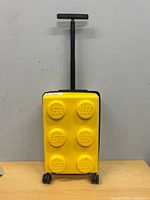 Front view of yellow LEGO suitcase showing six raised studs and telescopic handle