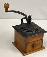 Full view of coffee grinder showing crank, cast-iron top, wood base, drawer