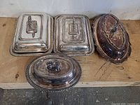 Four covered silver-plated serving dishes grouped on bench