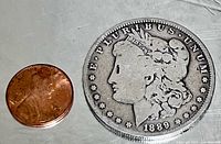 Obverse of 1889 Morgan dollar next to a penny for scale