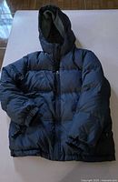 Front view of dark charcoal GapKids hooded puffer jacket laid flat