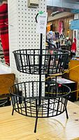 Full view of black metal tiered basket stand with two visible baskets and central rod