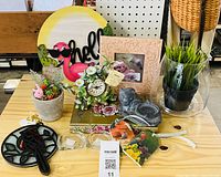 All items arranged on table: bird clock, flamingo sign, frame, floral clock, cat figurine, artificial plants, flower sprays, ribbons