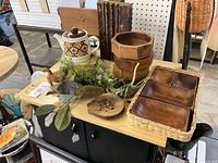 Overview of lot on tabletop including teapot, wooden bowls, tray in basket, trivet, bird figures, books and greenery