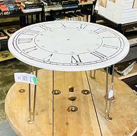 Overall view of round clock face table on folding hairpin legs