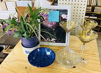 All items on wooden surface: framed floral print, three gold filigree martini glasses, blue ceramic bowl, clear pressed-glass bowl
