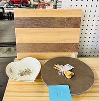 Striped wood cutting board, round grey riser, heart ceramic dish, four wooden spoons tied together