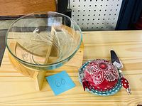 Glass bowl on wood stand next to red lidded serving dish and spreader