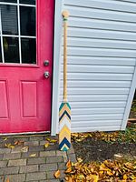 Full view of wooden paddle leaning against wall showing painted chevron blade and natural wood shaft