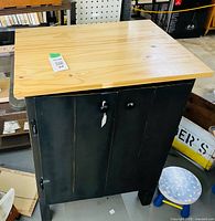 Front view of cabinet showing black painted body, pine top, metal knobs