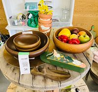 All items grouped on tabletop: nested wooden bowls, painted bowl with faux fruit, cast-iron shoe last, painted scissor holder, stacked terracotta pots visible in background