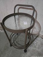 Full view of metal side table showing glass top shelf, frame, handle and casters