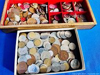 Two boxes containing mixed coins; wooden box above, cardboard tray below