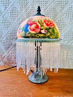 Full view of lamp showing painted shade, beaded fringe and base