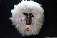 Front view of wool sheep showing full fluffy body, wooden face, felt ears, ribbon and bell