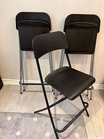 Front view of three folding bar stools, one unfolded in front