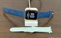 Front view of Apple Watch on stand with blue band and spare green band visible