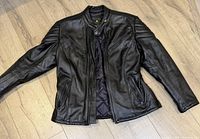 Full front view of black leather motorcycle jacket laid flat