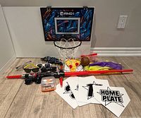 Group shot showing all items including mini hoop, ball, lightsaber, bases, sunglasses, goggles, Boggle, band, plush toy