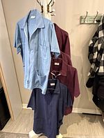 Five Aviva scrub shirts hanging on hooks displaying colors and overall style