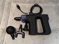 Massage gun with cable and three attachments laid on fabric surface