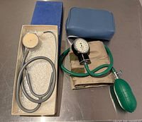 Stethoscope in original box next to blood pressure cuff set with blue case