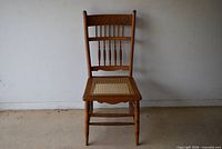 Front view of wooden chair showing cane seat, turned legs and spindled backrest