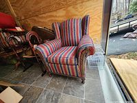 Front angle of striped wingback armchair showing upholstery and carved arm detail