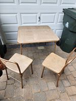 Square beige vinyl top card table with two matching chairs on patio pavers