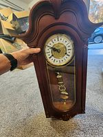 Front view of cherry wood wall chime clock showing dial, glass door, pendulum