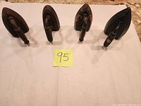 Four sad irons standing on soleplates, showing handles and size order