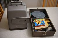 Projector carry case closed beside open film storage tray showing reels and boxed films