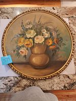 Front view of round floral painting in gilt frame