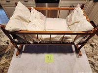 Overall view of wooden doll crib with pillows