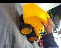 Side view of yellow plastic dump truck toy held by hand