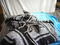 Black and white woven hoodie lying folded next to blue backpack