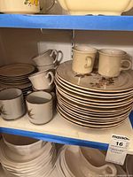 Shelf view showing stacks of dinner plates, saucers, assorted mugs and a creamer
