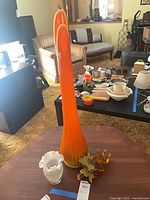 Tall ribbed orange-yellow gradient glass vase beside amber glass grapes on table