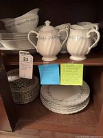 China pieces displayed on cabinet shelves including creamer, sugar bowl, cups, saucers, serving bowls