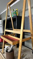Front view of wood A-frame easel showing top clamp and red-lined tray