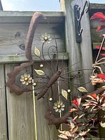 Front view of metal butterfly wall hanging showing rust-brown finish, floral and leaf accents, scroll wing design