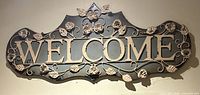 Front view of entire metal WELCOME sign showing lettering and floral scrollwork
