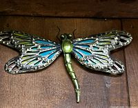 Green-blue metal dragonfly wall plaque on wood background