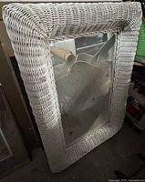 Front view of rectangular mirror with off-white wicker frame leaning against wall