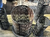 Four black metal filigree candle holders of varying sizes on wooden surface