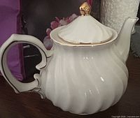 Left profile of white porcelain teapot showing fluted body, handle and spout