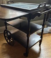 Angled view of wooden rolling cart showing shelves, spoked wheel, casters and removable tray on top