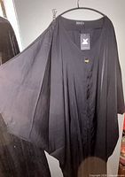 Full view of black kimono-style duster on hanger with XPLUSWEAR tag attached