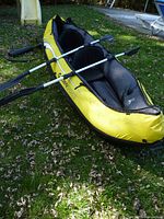 Side view of yellow two-person inflatable kayak with two paddles and seats installed