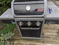 Front view of Coleman 3-burner gas grill showing controls, thermometer, side shelves